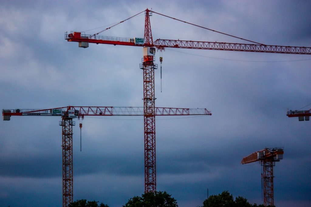 Tower cranes stand tall under a dramatic cloudy sky, representing modern industry.