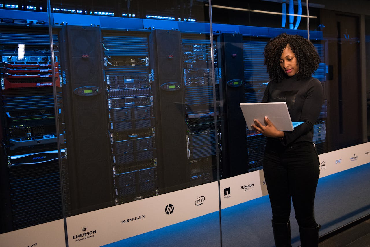 services-01 A female engineer using a laptop while monitoring data servers in a modern server room.