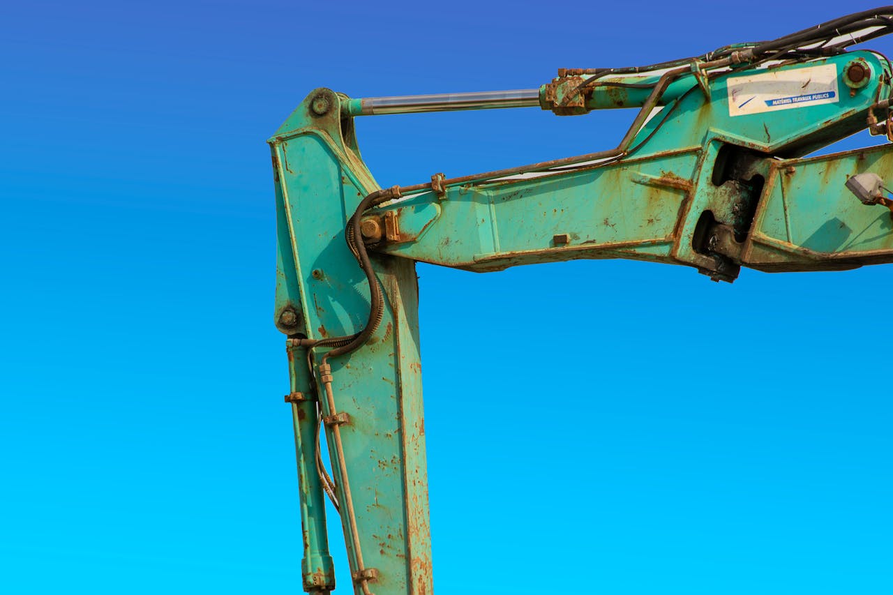 gallery-2 Detailed view of a turquoise excavator arm against a vivid blue sky.