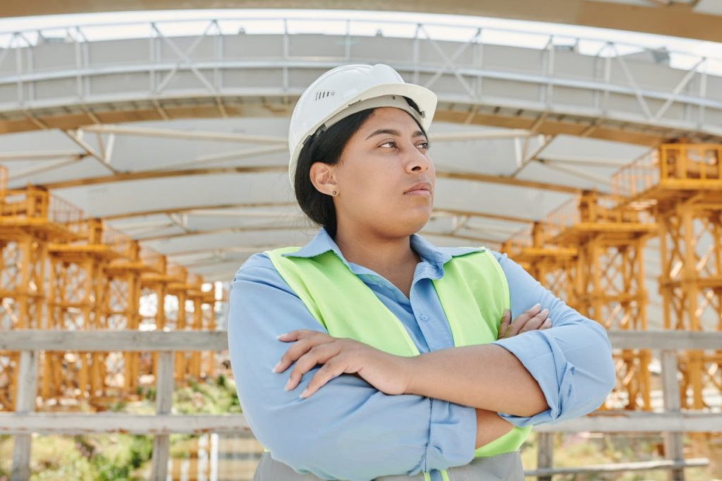 The Art of Drawing Readers In: Your attractive post title goes here Young female engineer crossing her arms at a construction site, wearing a hardhat and reflective vest.