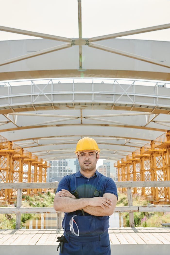gallery-1 Male construction worker with crossed arms at a bridge site with orange scaffolding.